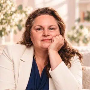 Nicole Quast-Prell – Autorenporträt Nicole Quast-Prell sitzt auf einem Sofa und stützt nachdenklich ihr Gesicht auf eine Hand.